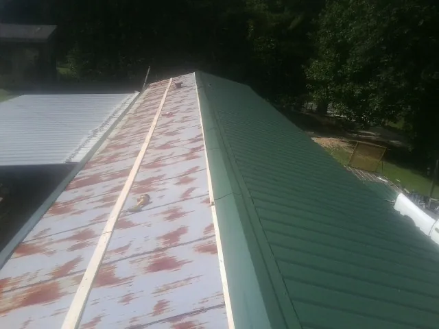Old rusted panels beside newly installed green metal roofing — Wind Damage Roof Repair by Roofing Brothers in Iona