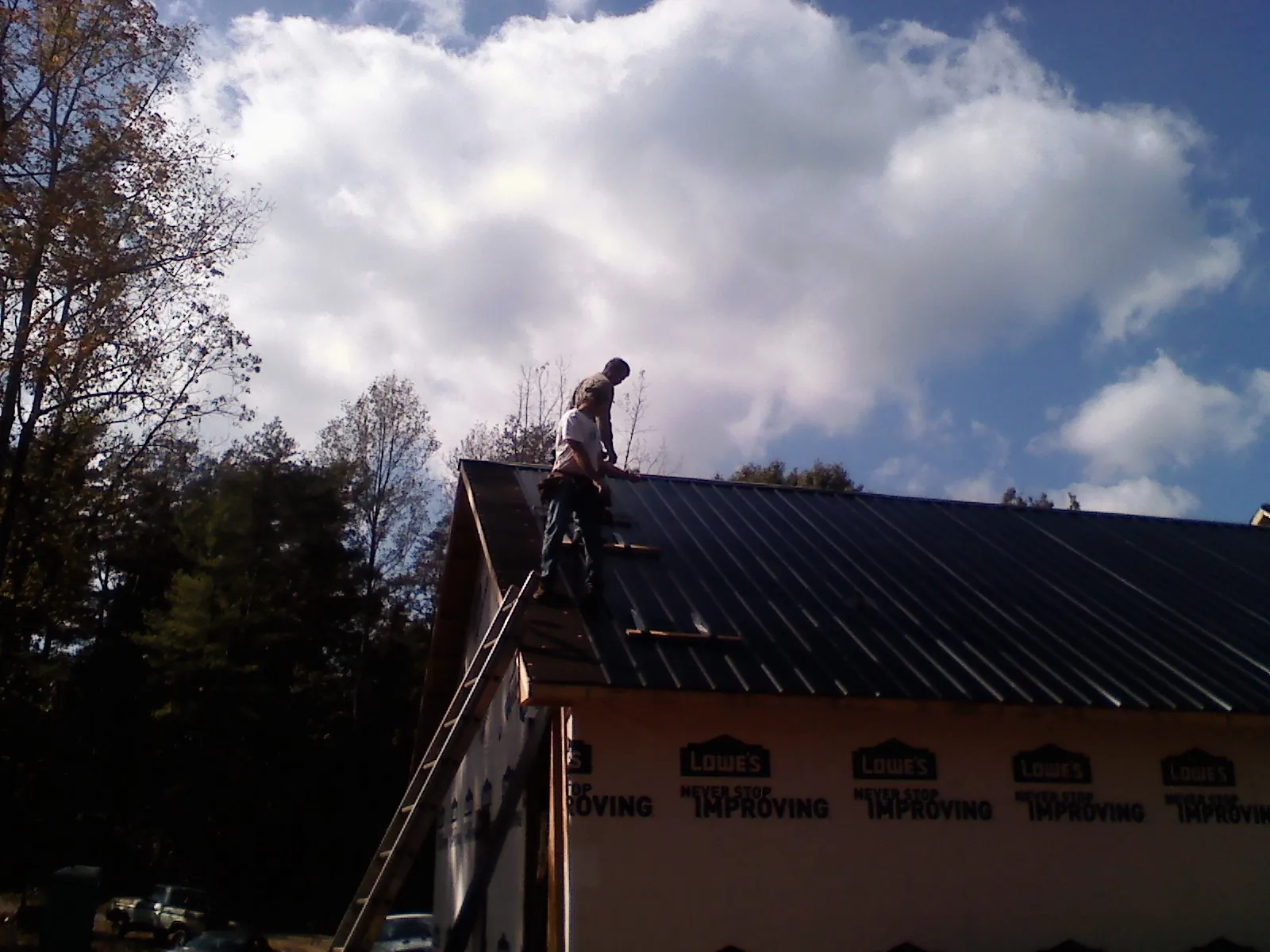 Roofer fastening dark metal panels high against a cloudy sky, from a Roof Inspection job in Iona