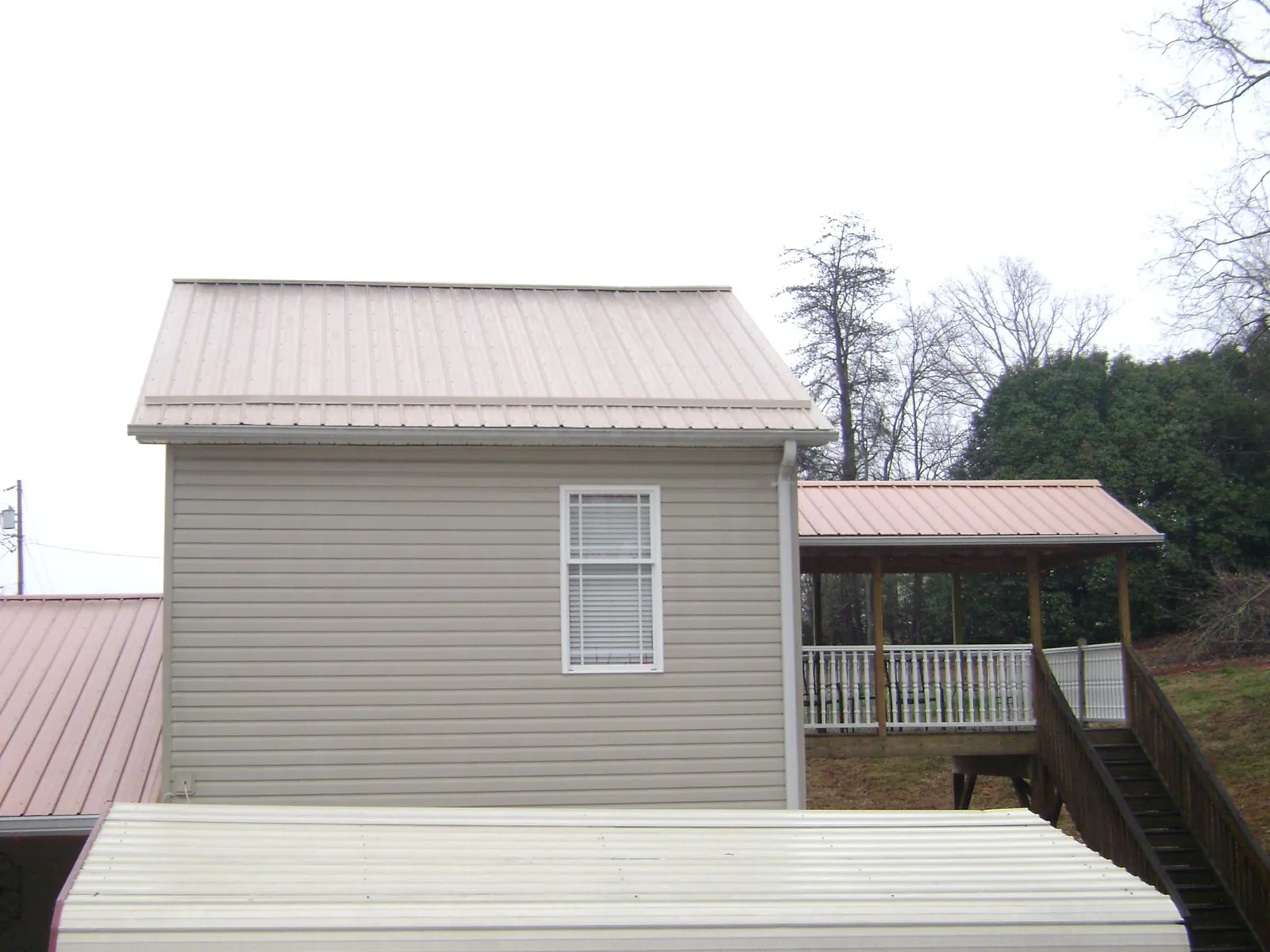 Tan metal roofs on a two story addition and attached porch, from a Roof Replacement job in Iona